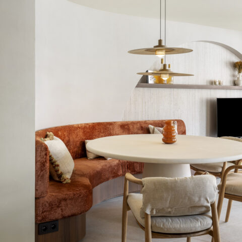 Eethoek met een gebogen zitbank in terracotta velours op notelaar voet en een ronde tafel onder hanglampen, maatwerk van YVES.