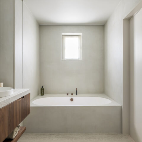 Badkamer met ingebouwd bad in een naadloze wandafwerking en een notelaar badmeubel met natuurstenen blad, maatwerk van YVES.