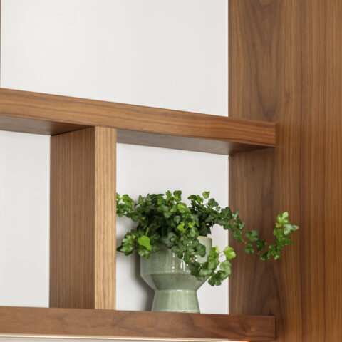 Detail van een wandrek in notelaar met verticale stijl en ledlijn onder de plank, maatwerk van YVES Interieur Op Maat.