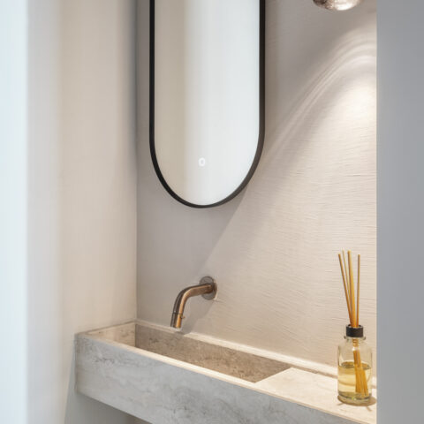Fonteintje in natuursteen met wandkraan in brons, ovale spiegel en hanglamp in een toilet, maatwerk van YVES.