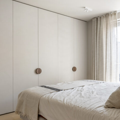 Slaapkamer met greeploze kastwand in de wandkleur en ronde notelaar grepen, naast linnen gordijnen.