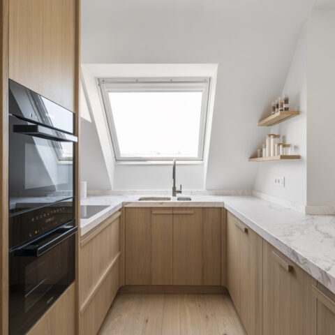 U-vormige keuken in lichte eik met marmeren werkblad onder een dakraam en zwevende eiken legplanken, maatwerk van YVES.