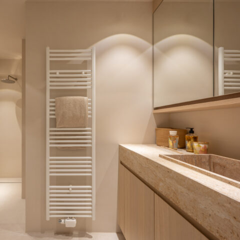 Badkamer met massieve travertin wastafel op een eiken onderkast, spiegelkast en handdoekradiator in Knokke.