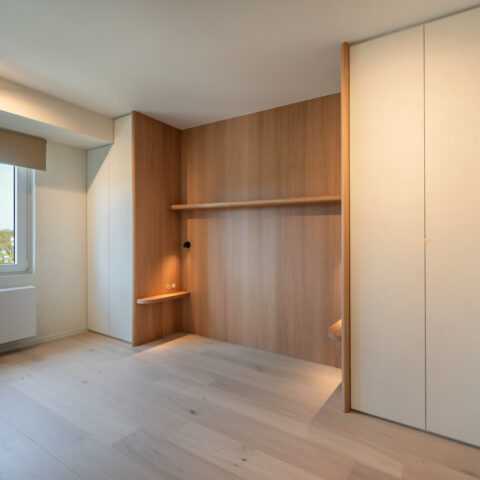 Bednis in eiken wandbekleding met leeslampjes en nachtplankjes, ingebouwd tussen greeploze witte maatkasten.