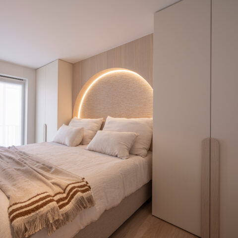 Boogvormig hoofdbord met indirecte ledverlichting en greeploze kastwand in een rustige slaapkamer.