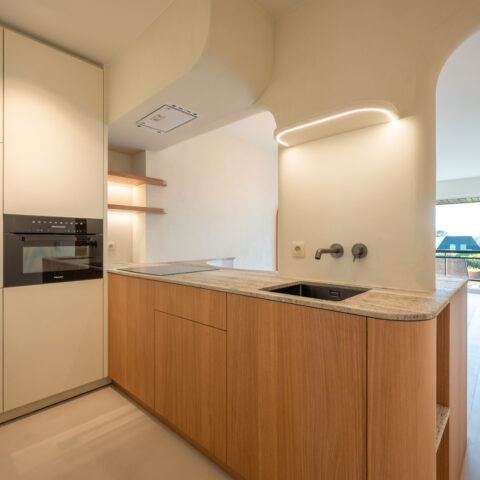 Keuken met eiken onderkasten, travertin werkblad en een gebogen kalkpleister plafond met verlichte nis, maatwerk van YVES.