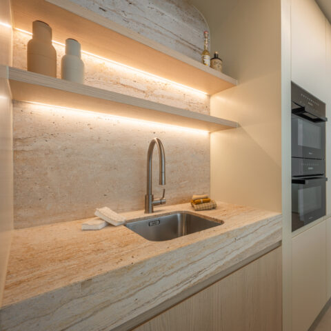 Kitchenette met massief travertin werkblad en achterwand, verlichte eiken legplanken en ingebouwde Miele-ovens.