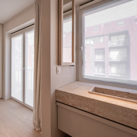 Lavabomeubel in travertin met ingewerkte wastafel onder het raam van de slaapkamer, Knokke.