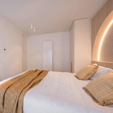 Slaapkamer met boogvormig hoofdbord en geïntegreerde ledverlichting, zijaanzicht in appartement Parmentierlaan.