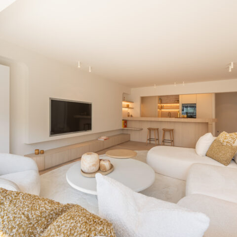 Zithoek met zwevend tv-meubel en verlichte keukenwand in lichte eik, maatwerk van YVES Interieur Op Maat.